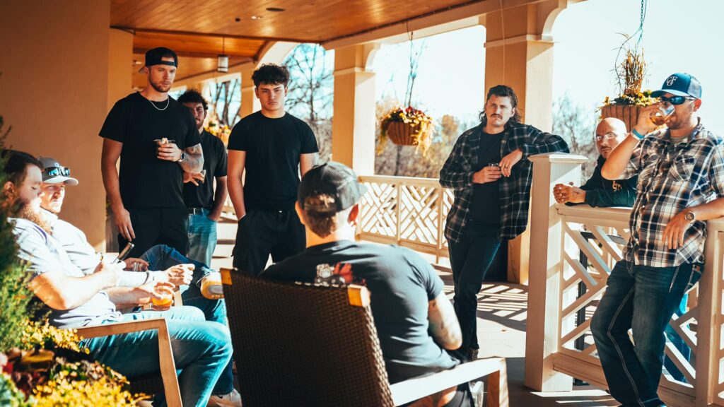 A group of men gathered on a sunlit porch, deep in conversation about discipline, accountability, and personal growth at an Uncaged Men’s Accountability Group event.