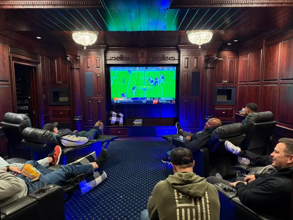 Group of men in a luxury theater-style room watching a football game, engaging in brotherhood, relaxation, and strategic discussions at an Uncaged event.
